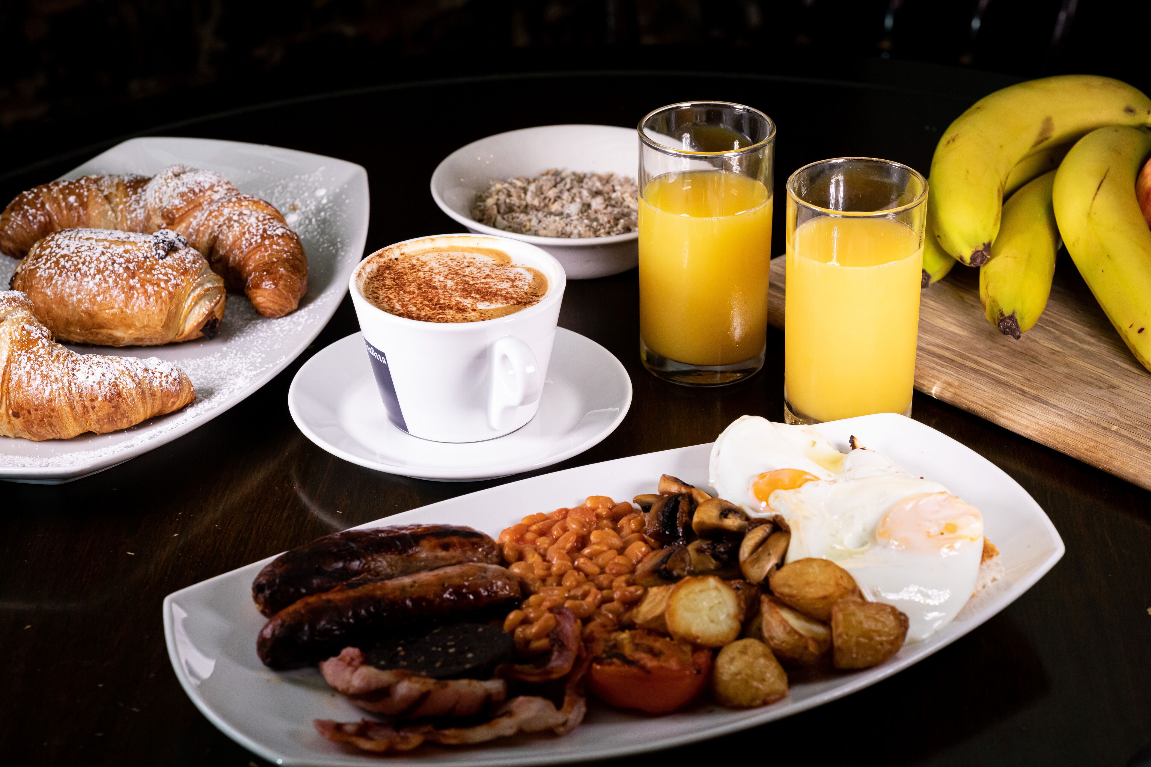 A breakfast plate with croissants, coffee, beans, eggs, sausages, and toast.