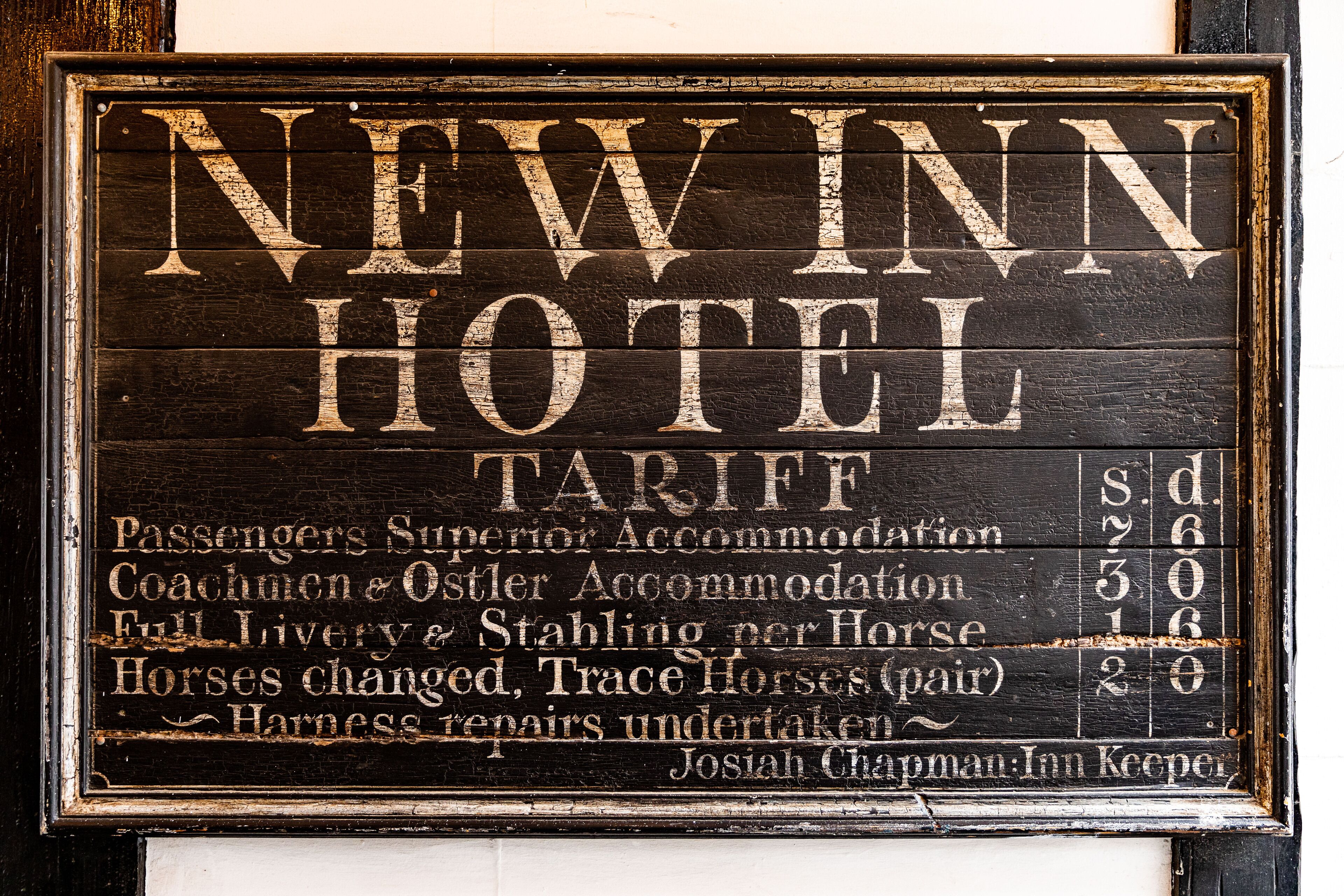 Un letrero antiguo del Hotel New Inn con una lista de tarifas para diferentes servicios.