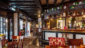 A bar area with wooden furniture, a patterned carpet, and a chalkboard menu. - The New Inn by Roomsbooked (Gloucester)
