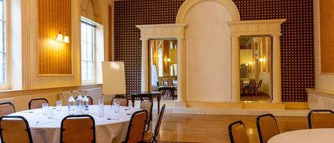 Un comedor de hotel con una mesa redonda dispuesta para una comida, rodeada de sillas y una araña colgante.