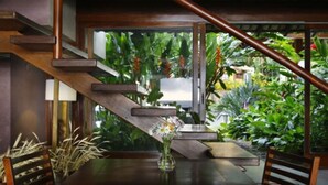 A dining area with a wooden table and chairs, a vase with flowers, and a staircase with a view of lush greenery. - Maitei Hotel (Porto Seguro)