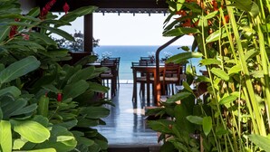 A covered outdoor dining area with tables and chairs, leading to a view of the ocean. - Maitei Hotel (Porto Seguro)