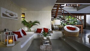 A modern living room with a sofa, a round wicker chair, a coffee table, and a staircase leading to an outdoor area. - Maitei Hotel (Porto Seguro)