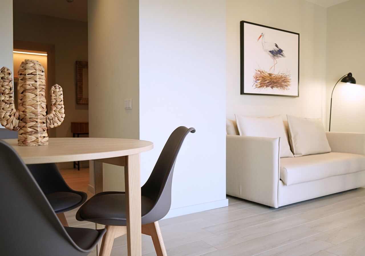 A modern living room with a white sofa, a dining table with chairs, and a framed artwork on the wall.