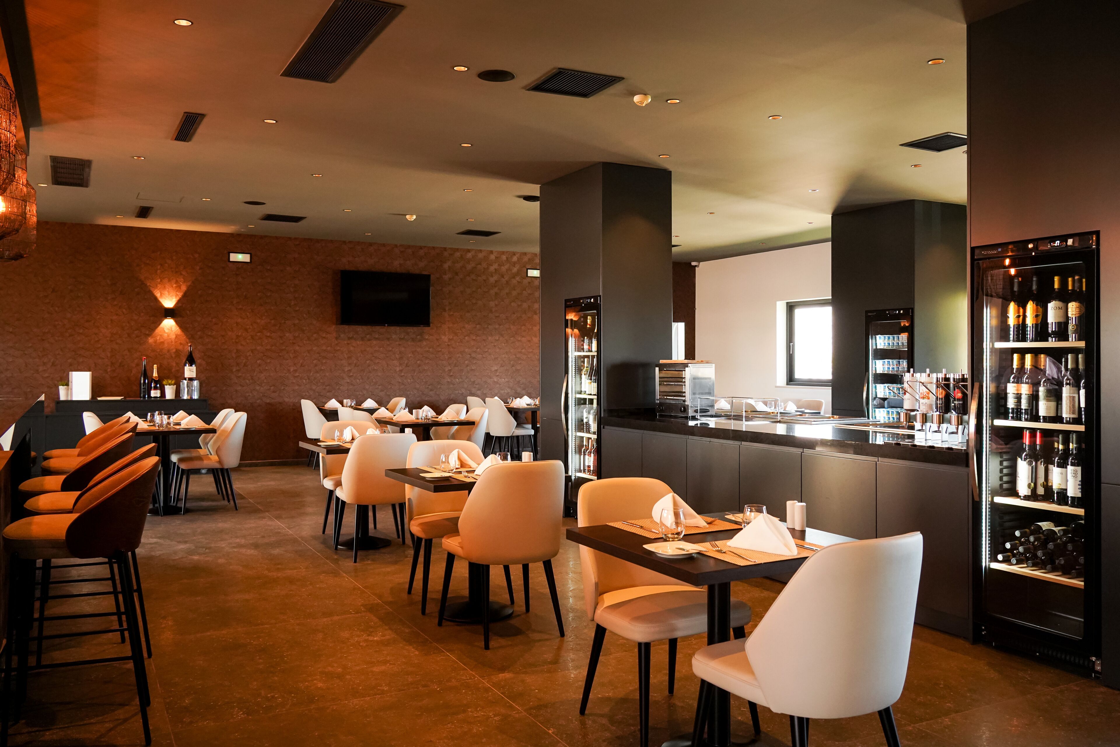 Ein Restaurant mit Tischen, Stühlen, einer Bar und einem Weinkühlschrank.