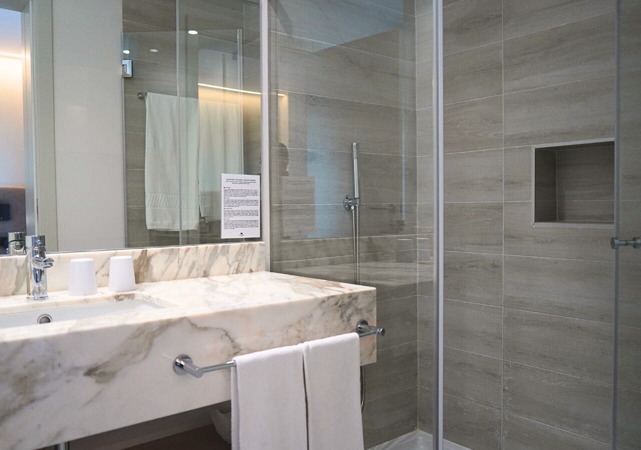 Une salle de bain moderne avec un lavabo en marbre, une cabine de douche en verre et un porte-serviettes.