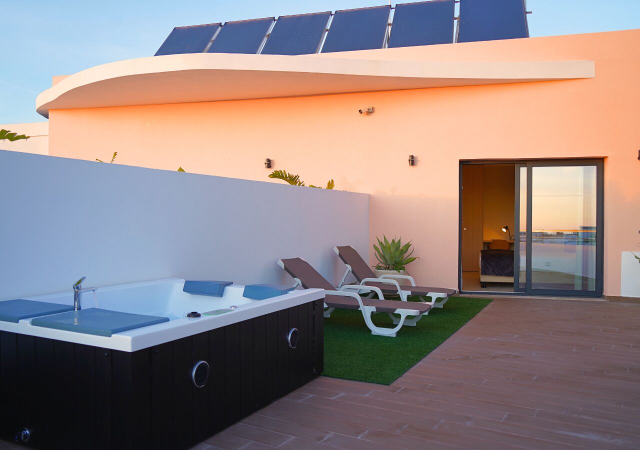 Un espace extérieur moderne doté d’un jacuzzi, de chaises longues et d’une porte vitrée donnant sur une pièce.