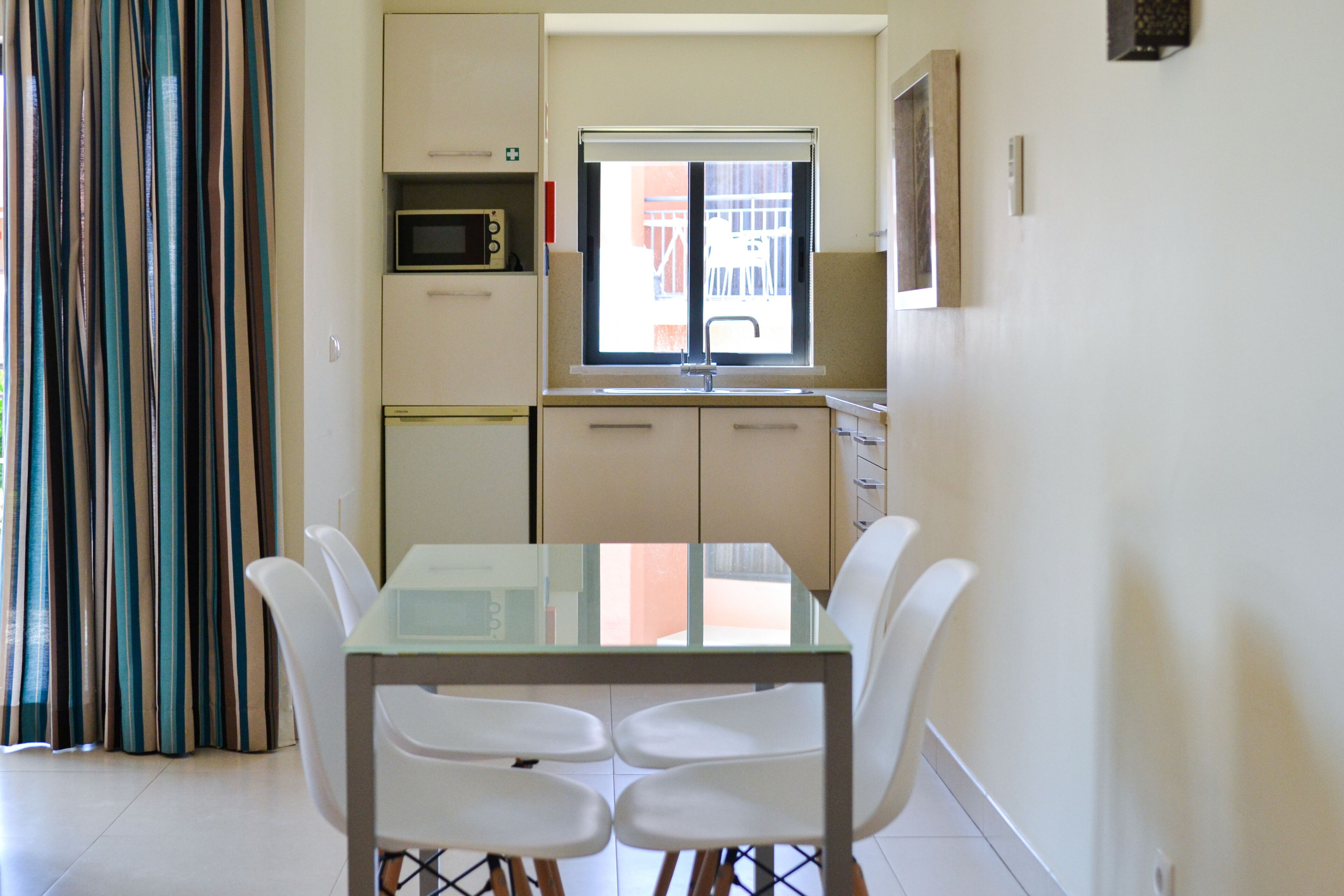 Een moderne keuken met een eettafel en stoelen, een magnetron, en een raam met uitzicht op buiten.