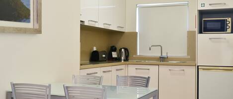 Una cocina compacta con una mesa de comedor y sillas, microondas, hervidor y cafetera.