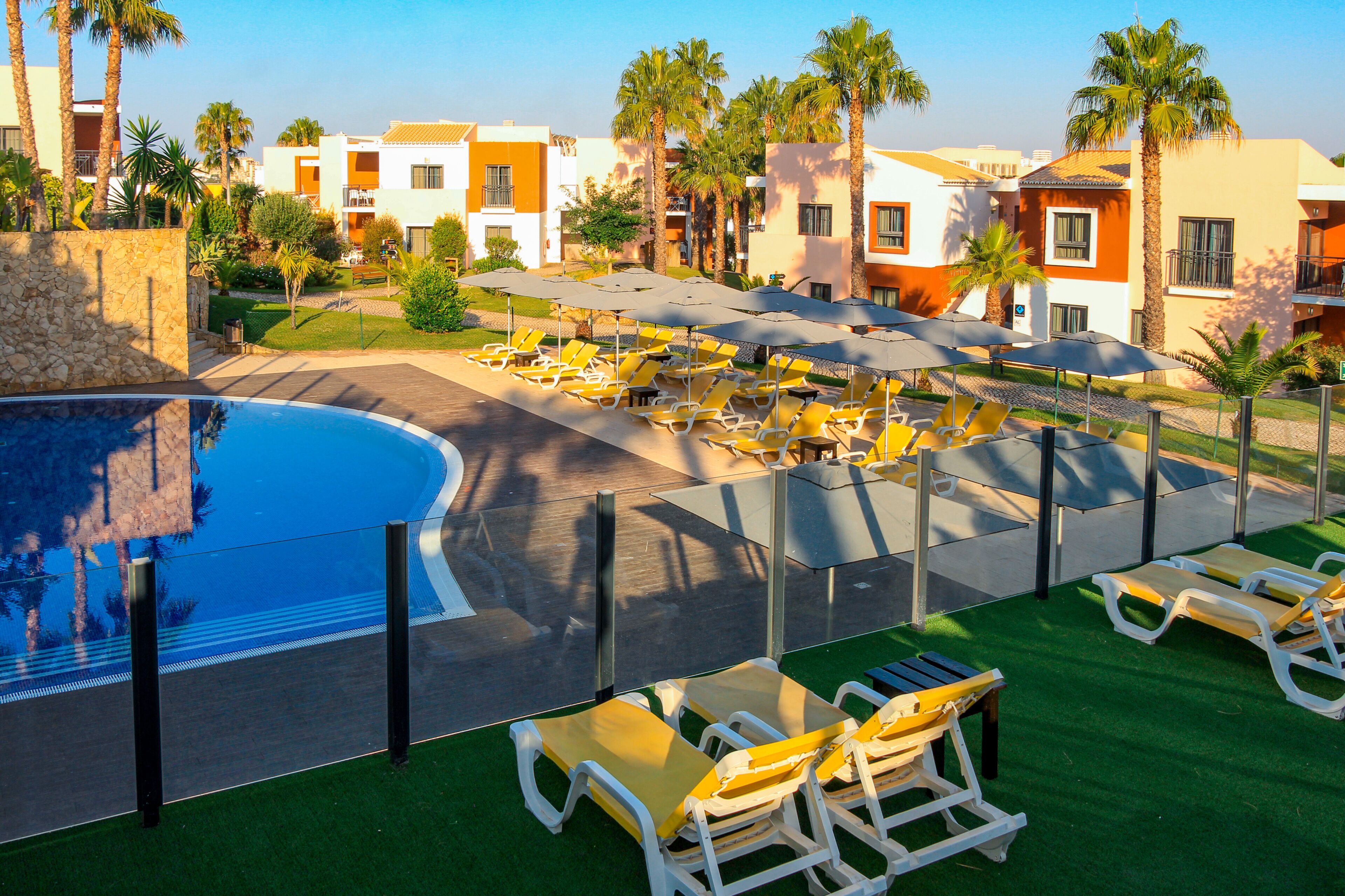 Een resort met een zwembad, ligbedden en een verzorgd gazon.