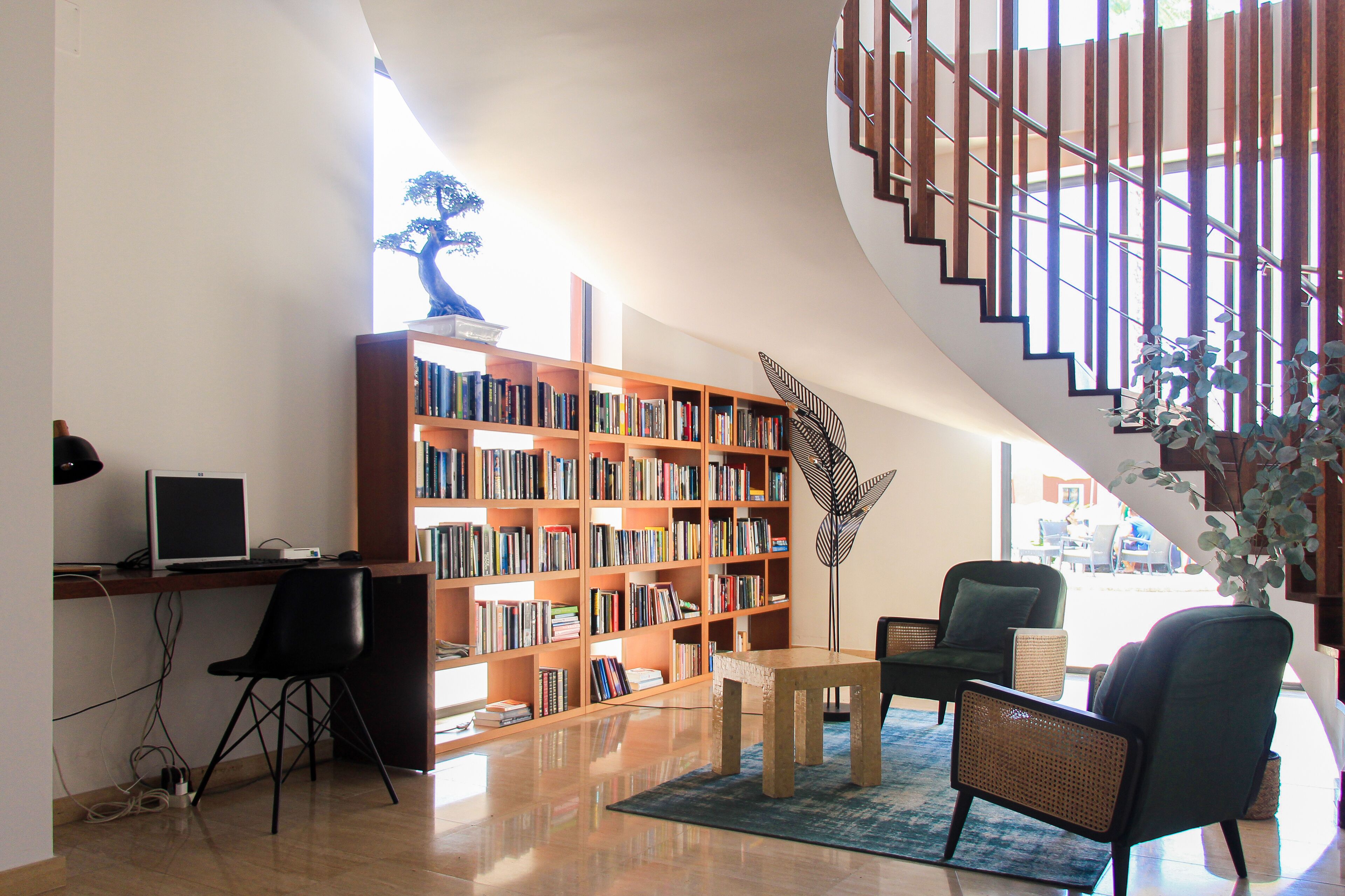A modern library with a large wooden bookshelf, a desk with a computer, and comfortable seating.