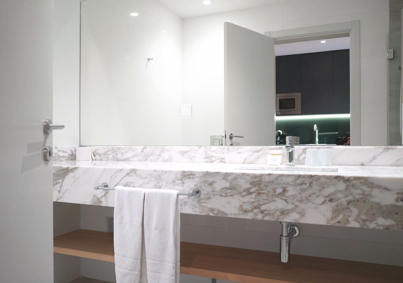 A modern bathroom with a marble countertop, a large mirror, and a towel rack.
