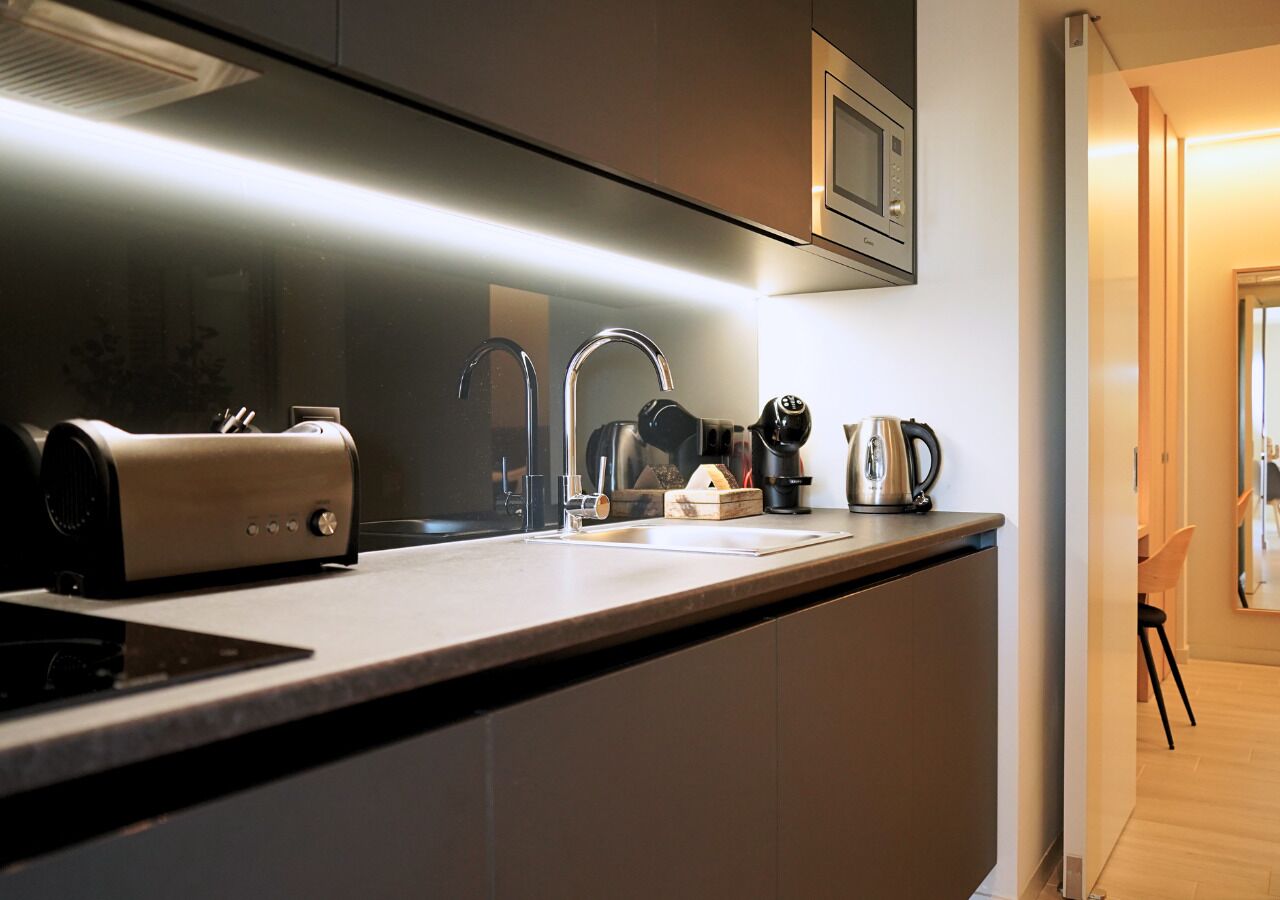 A modern kitchen with a built-in stove, a coffee maker, and a kettle on the counter.