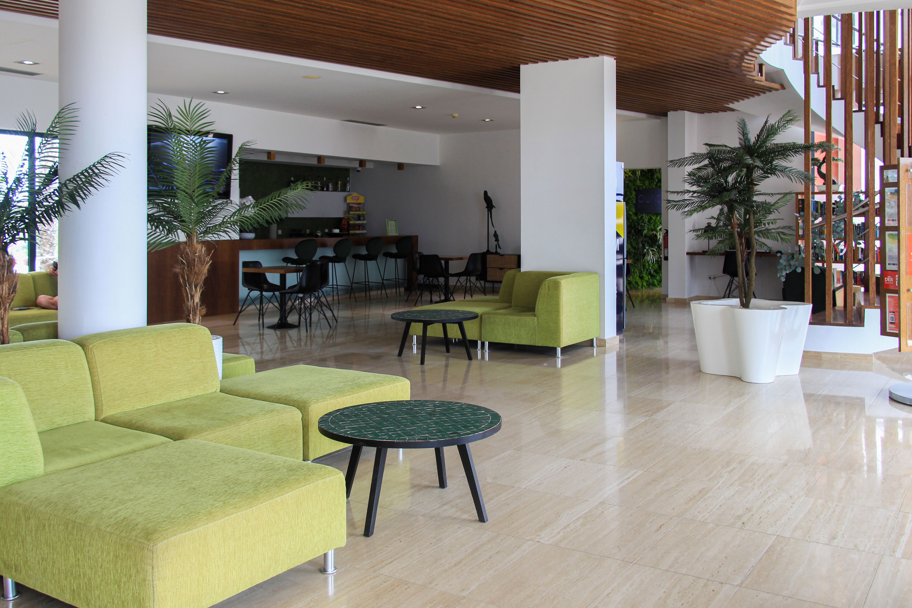 A modern lobby with green sofas, round tables, and potted plants.