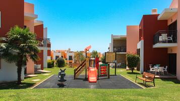 Children can play and climb in this outdoor play area surrounded by lush greenery and palm trees.