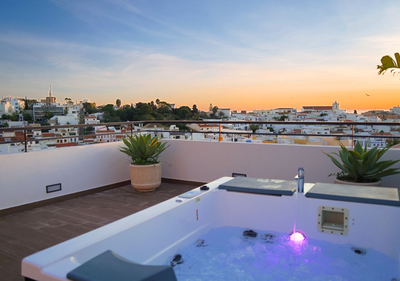 Une terrasse sur le toit avec un jacuzzi, des plantes en pot et une vue sur la ville au coucher du soleil.