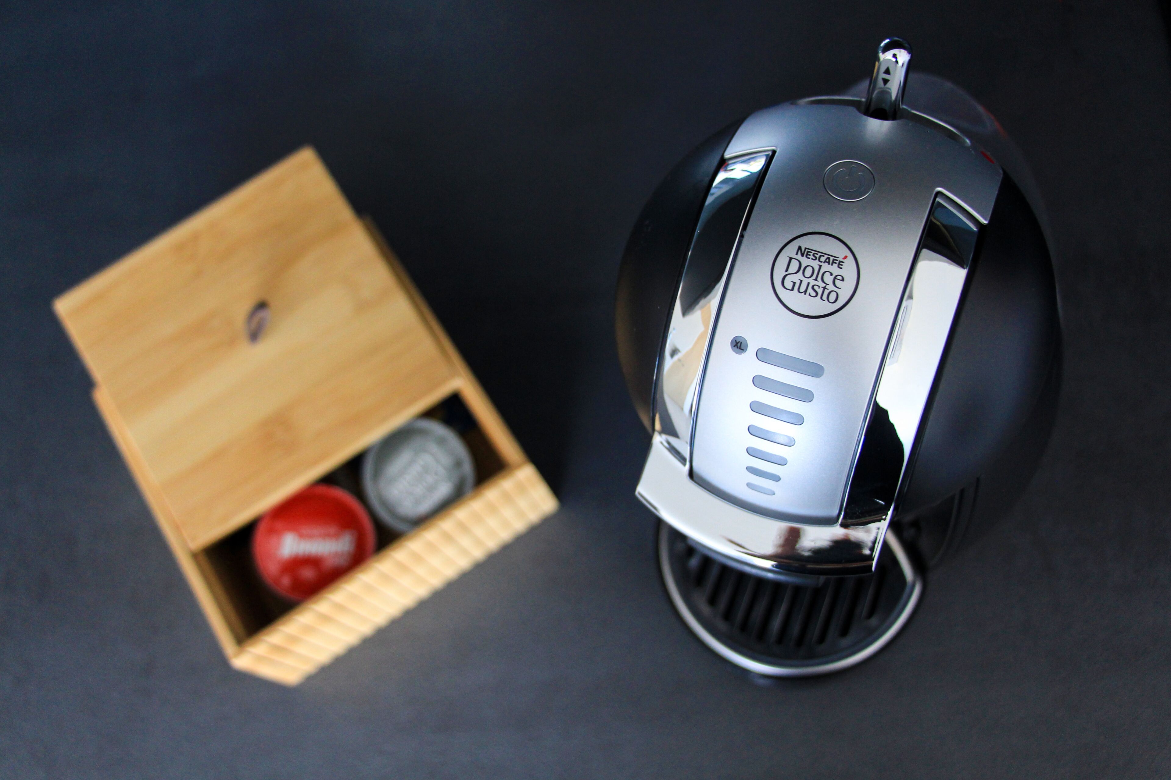 Eine Nescaf é Dolce Gusto Kaffeemaschine mit einer Holzkiste, die eine rote und eine silberne Kapsel enthält.