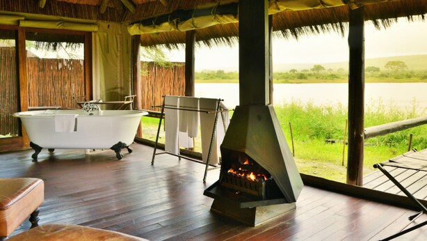Una habitación con bañera, chimenea y vistas a un campo cubierto de hierba.