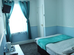 Een hotelkamer met een bed, een bureau met een afstandsbediening, een aan de muur bevestigde televisie en een raam met gordijnen.