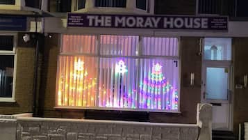 Um edifício com uma placa indicando 'THE MORAY HOUSE' e uma vitrine com decorações iluminadas.