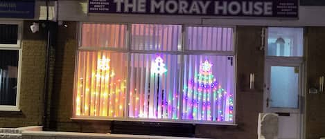 A building with a sign reading 'THE MORAY HOUSE' and a window display featuring illuminated decorations.