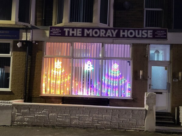Een gebouw met een bord waarop 'THE MORAY HOUSE' staat en een etalage met verlichte decoraties.