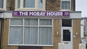 Een gebouw met twee verdiepingen, met een opvallend bord waarop 'The Moray House' staat, dat rechtstreekse boekingen aanprijst.