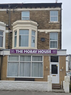 Een gebouw met twee verdiepingen, met een opvallend bord waarop 'The Moray House' staat, dat rechtstreekse boekingen aanprijst.