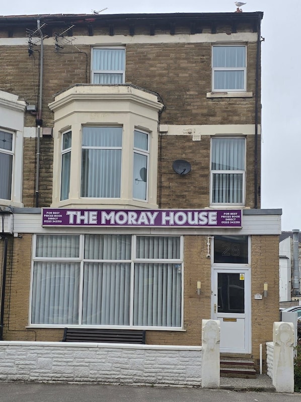 Een gebouw met twee verdiepingen, met een opvallend bord waarop 'The Moray House' staat, dat rechtstreekse boekingen aanprijst.