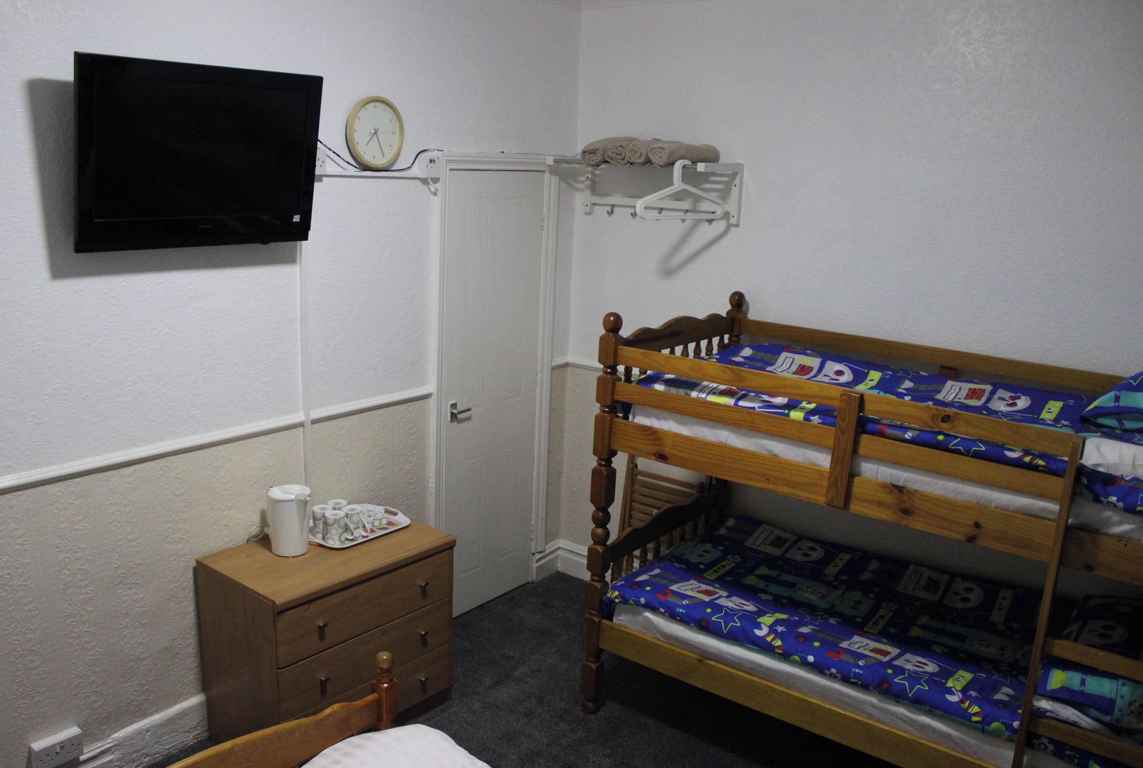 A bedroom with a bunk bed, a bedside table with a lamp, a wall-mounted TV, and a door.