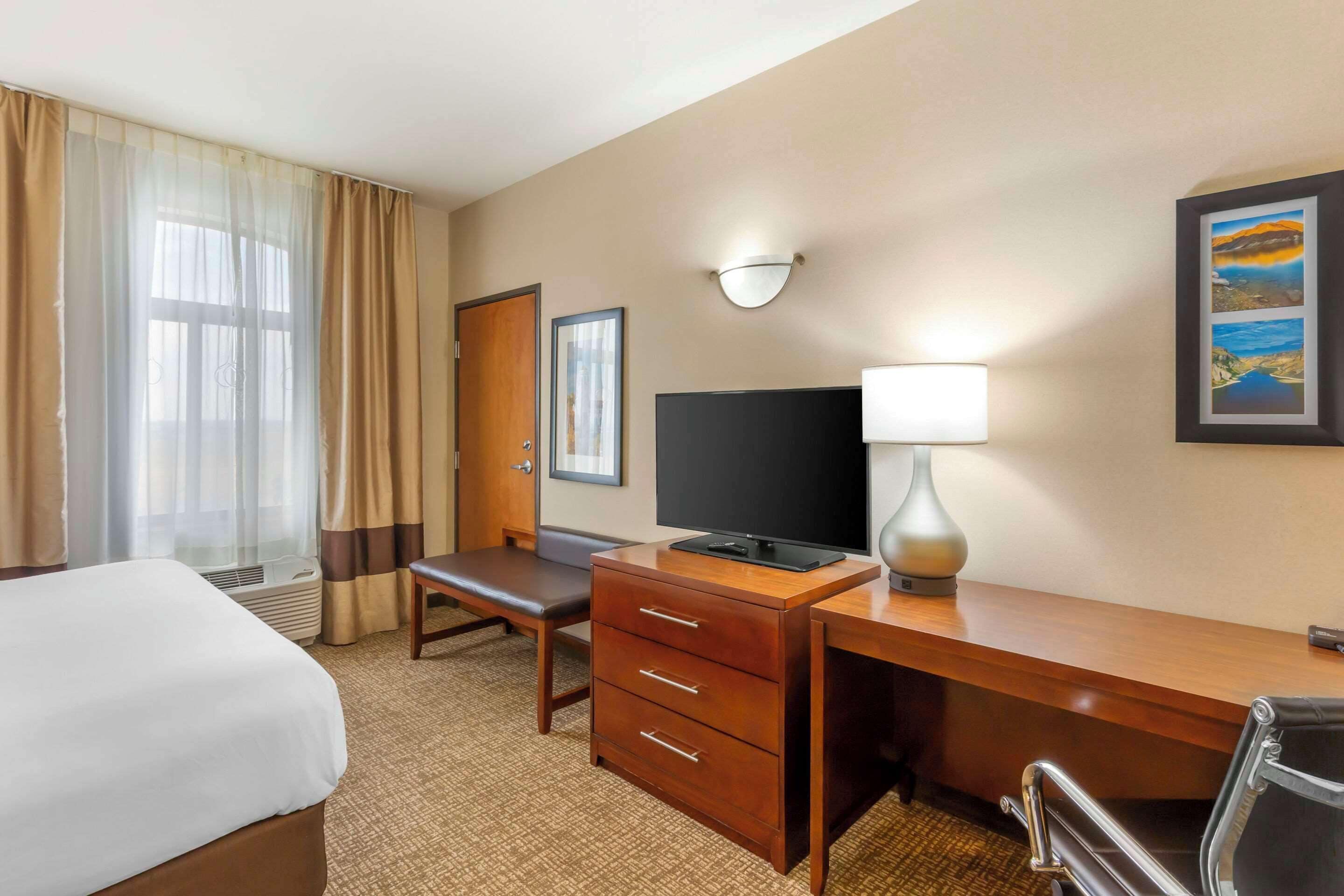 A hotel room with a bed, a desk with a television, a lamp, and a chair.