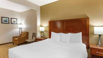 A hotel room with a large bed, a wooden headboard, a chair, a nightstand with a lamp, and two framed pictures on the wall.