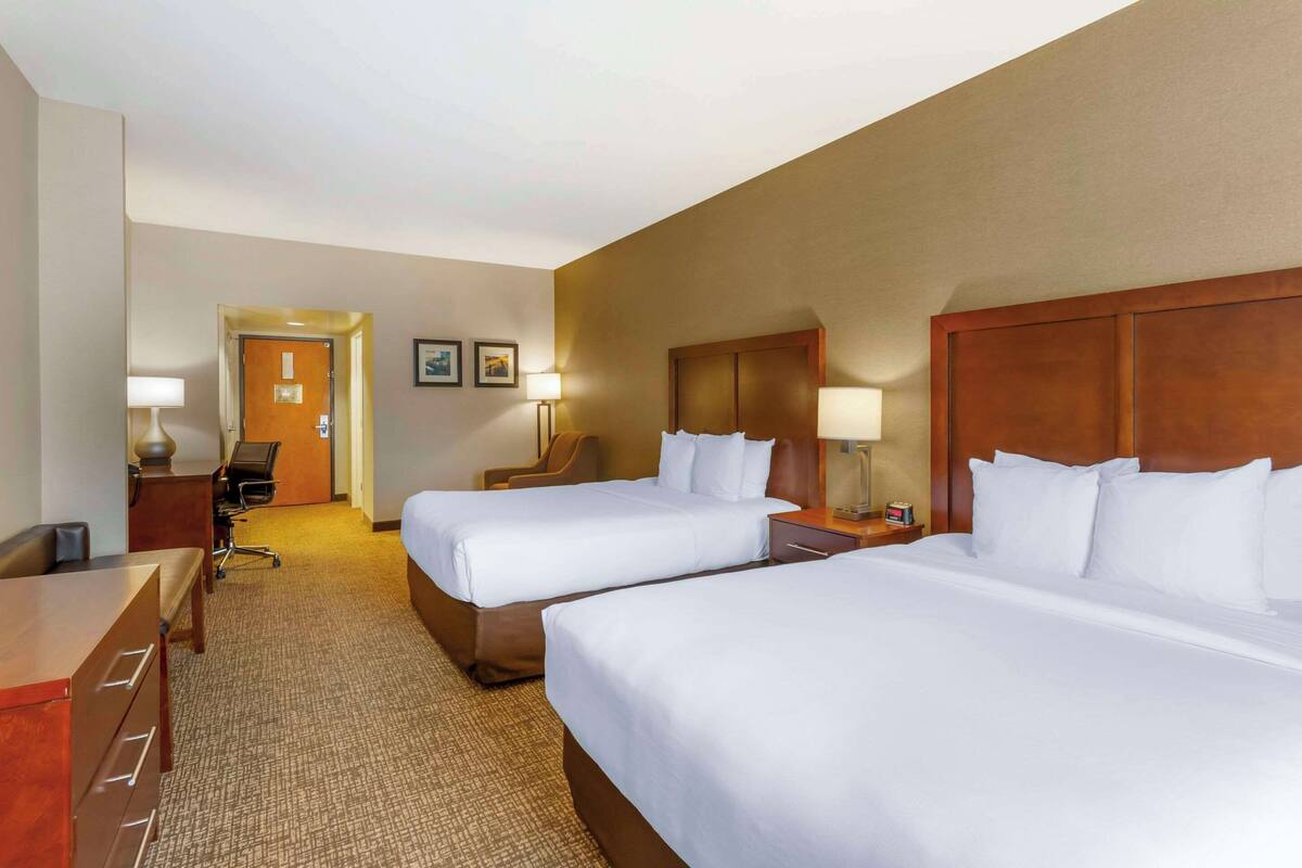 A hotel room with two beds, a desk, a chair, and a door leading to another room.