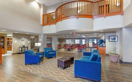A spacious lobby with blue sofas, a wooden staircase, and a dining area in the background.