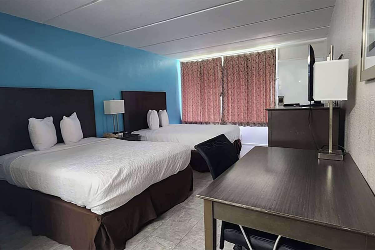 Une chambre d’hôtel avec deux lits, un bureau, une lampe et une fenêtre avec des rideaux.