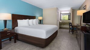 Habitación de hotel con una cama grande, mesitas de noche con lámparas, un escritorio con silla, televisión y un baño visible a través de una puerta abierta.