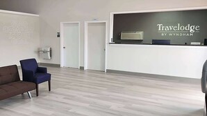 Un área de recepción con un letrero que dice "Travelodge by Wyndham" y un eslogan en la pared. Hay dos puertas, un sofá marrón y una silla azul.