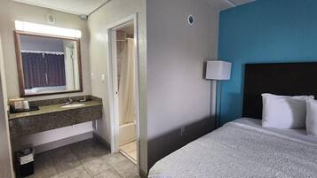 Une chambre d’hôtel avec un lit, une table de chevet, un miroir, un lavabo et une douche.