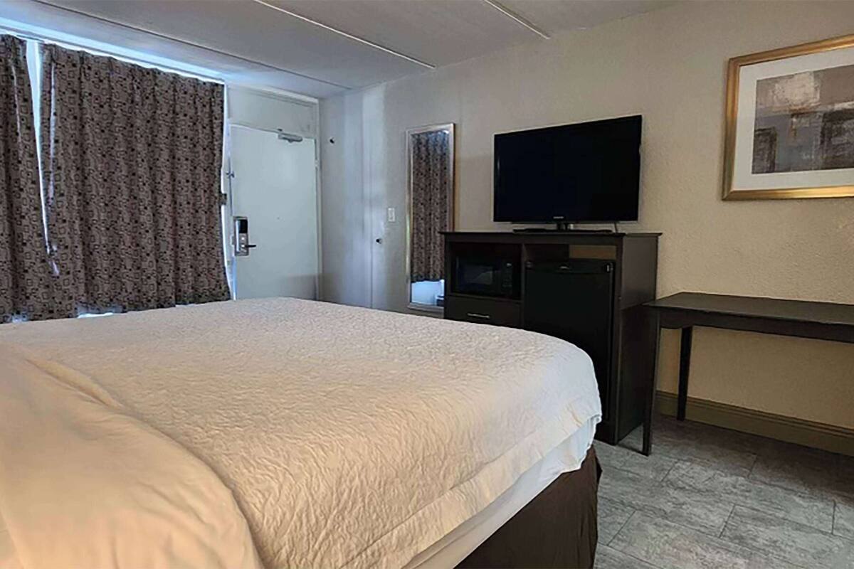 Une chambre d’hôtel avec un grand lit, un téléviseur à écran plat posé sur un meuble, un bureau et une porte.