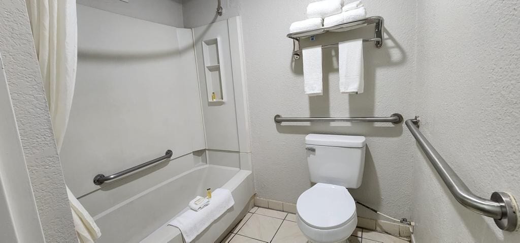 A bathroom with a bathtub, toilet, and handrails.