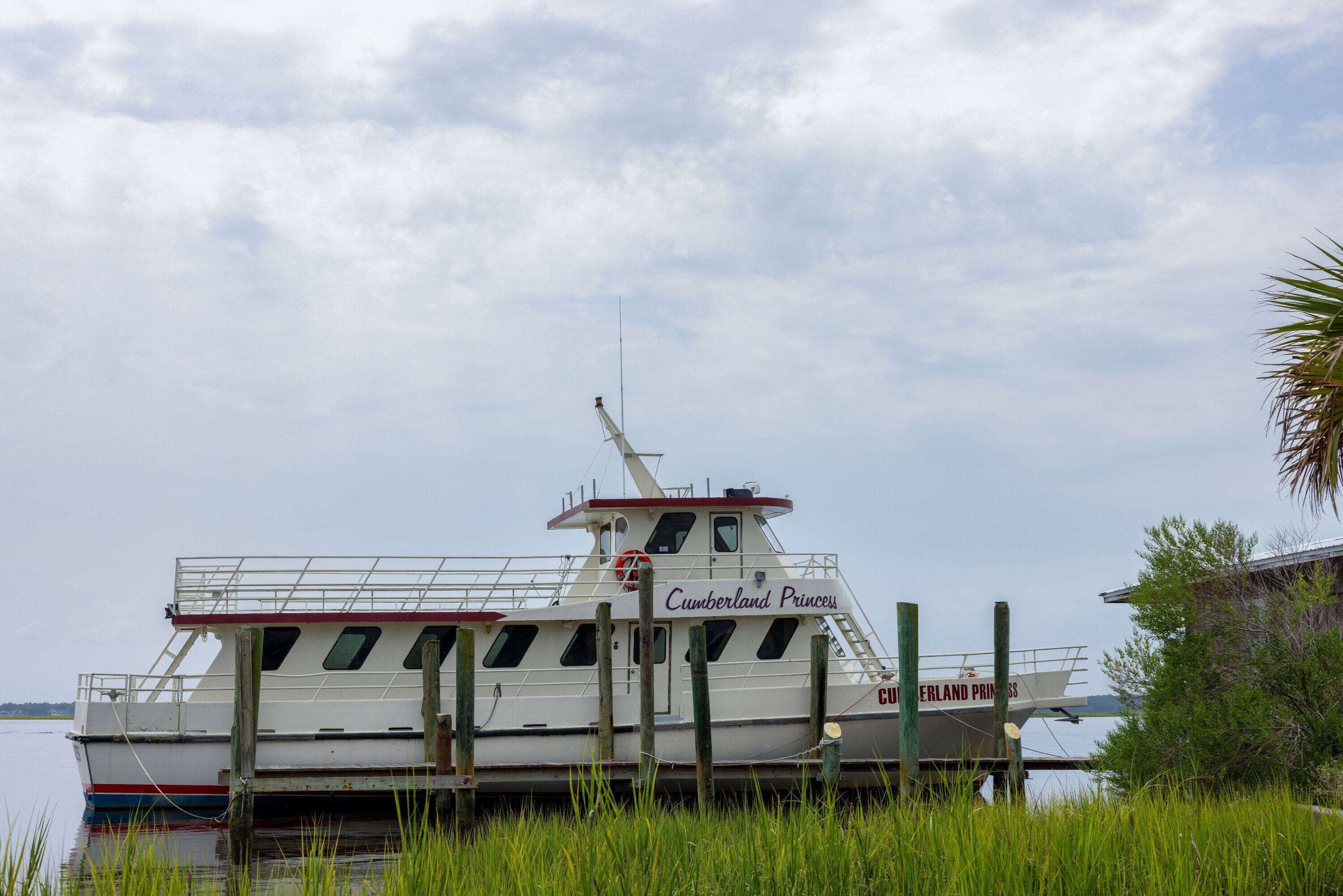 A boat named 'Cumberland Princess' docked at a pier with a grassy foreground and a cloudy sky in the background.