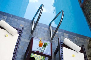 Un área junto a la piscina con dos sillones de descanso, una mesa de vidrio con una bebida y un plato de comida, y una vista despejada de la piscina.