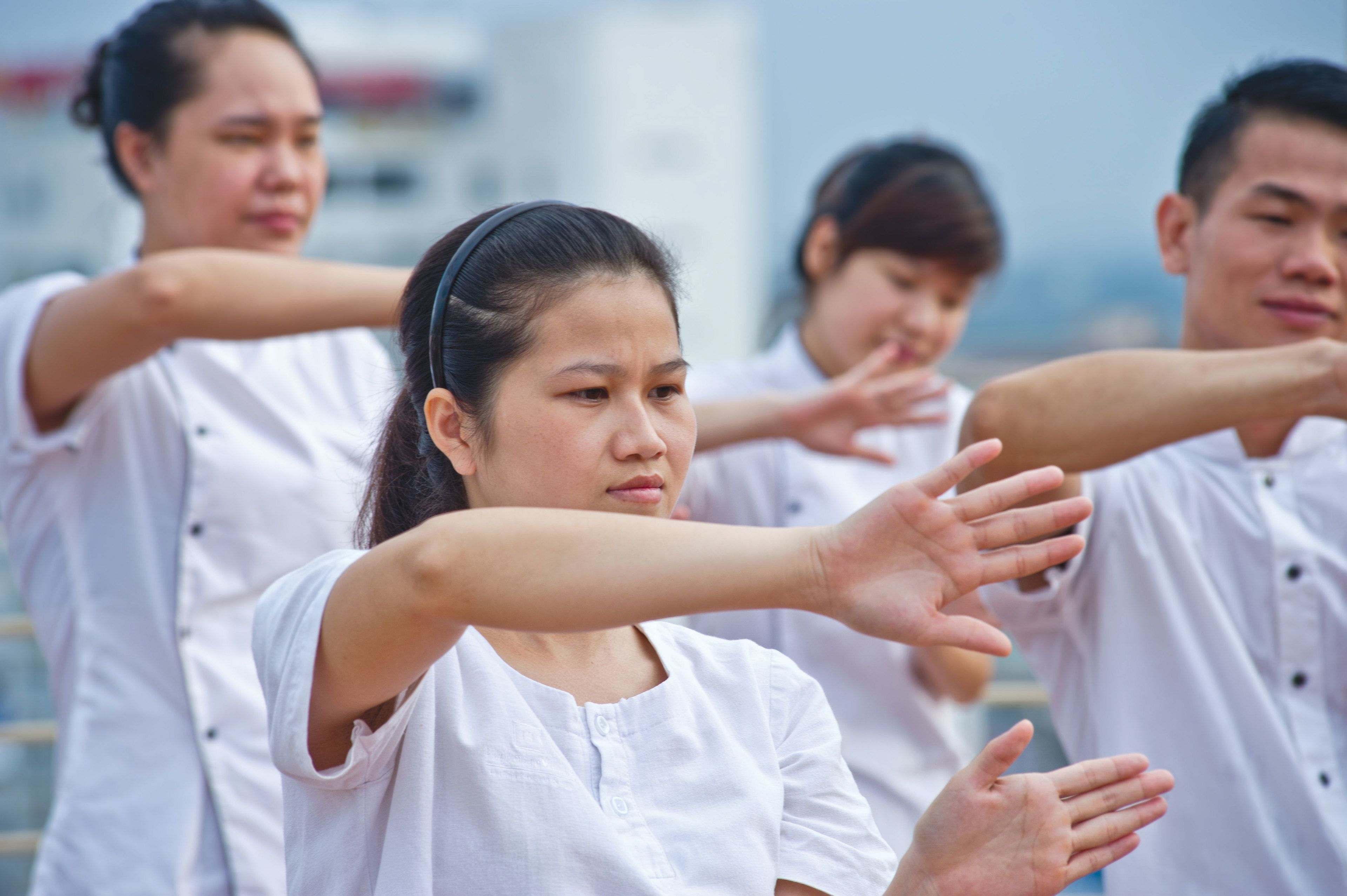 A group of people in white shirts performing a stretching exercise outdoors.
