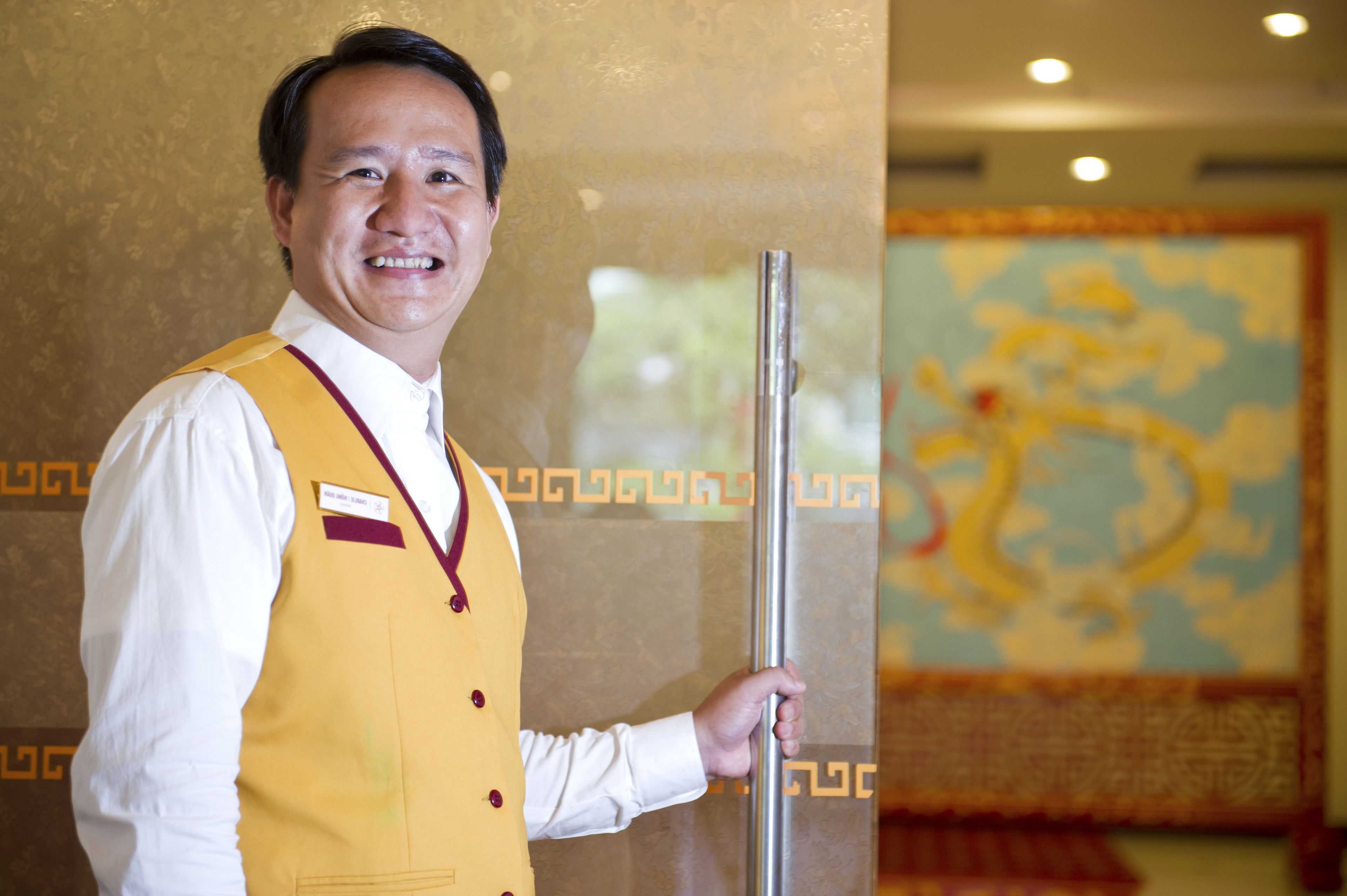 A man in a yellow vest standing in a room with a decorative wall mural.