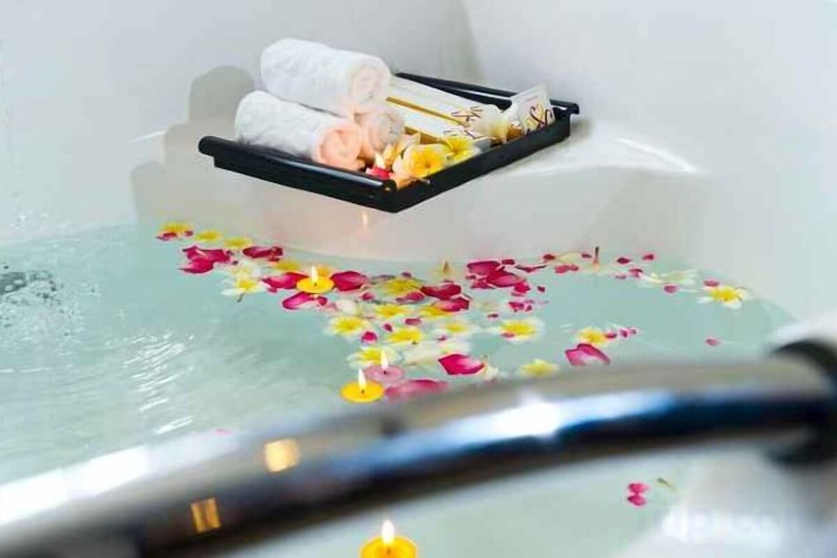 Una bañera con pétalos de rosa y una vela.