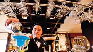 Ein Barkeeper gießt ein Getränk in ein Martini-Glas ein.