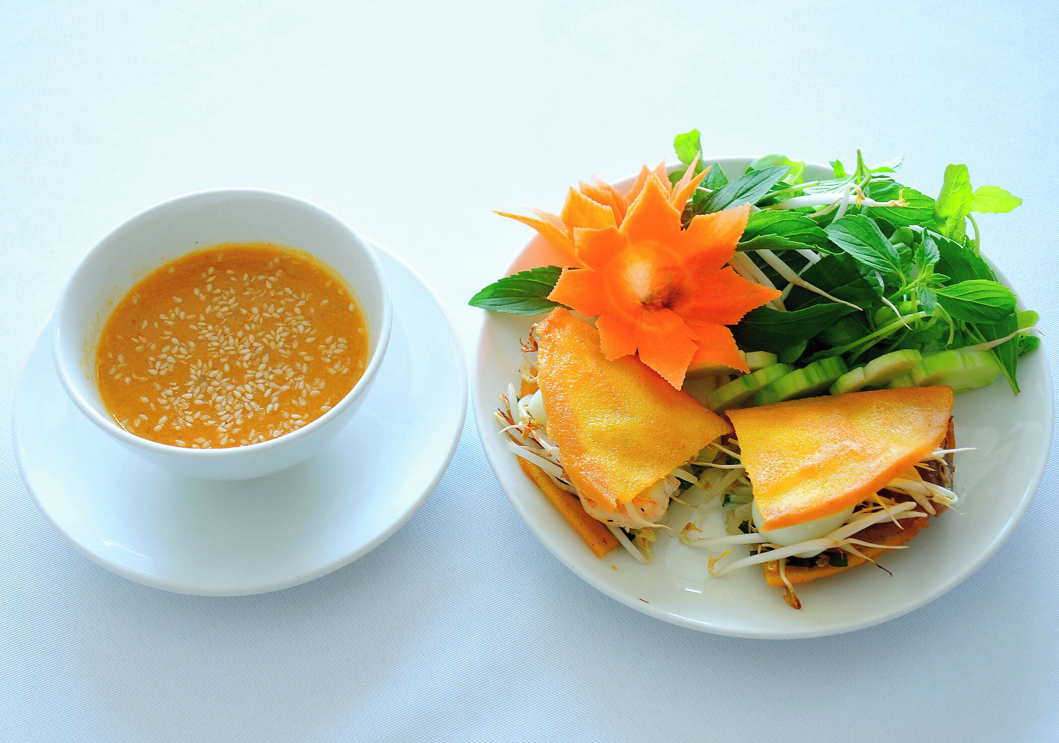 A white bowl of soup with sesame seeds and a plate of vegetable sandwich with sprouts and herbs.