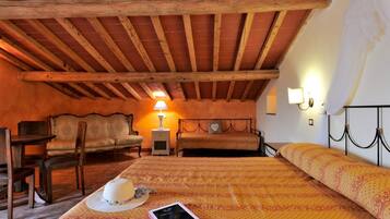 Una camera da letto mansardata accogliente, con travi a vista in legno, un letto con lenzuola a motivi decorativi, un comodino con una lampada, una sedia e un tavolino.