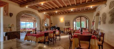 Un restaurante con varias mesas, vigas de madera en el techo y paredes de piedra.