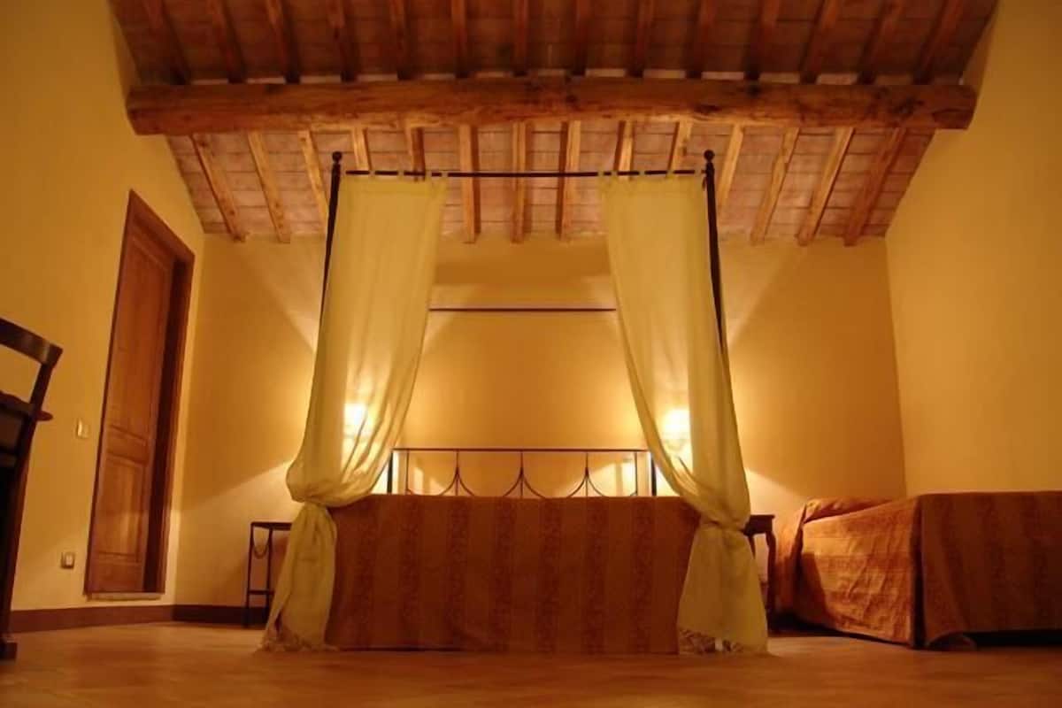 Una stanza con soffitto in legno, un letto con testiera e una finestra con tende.
